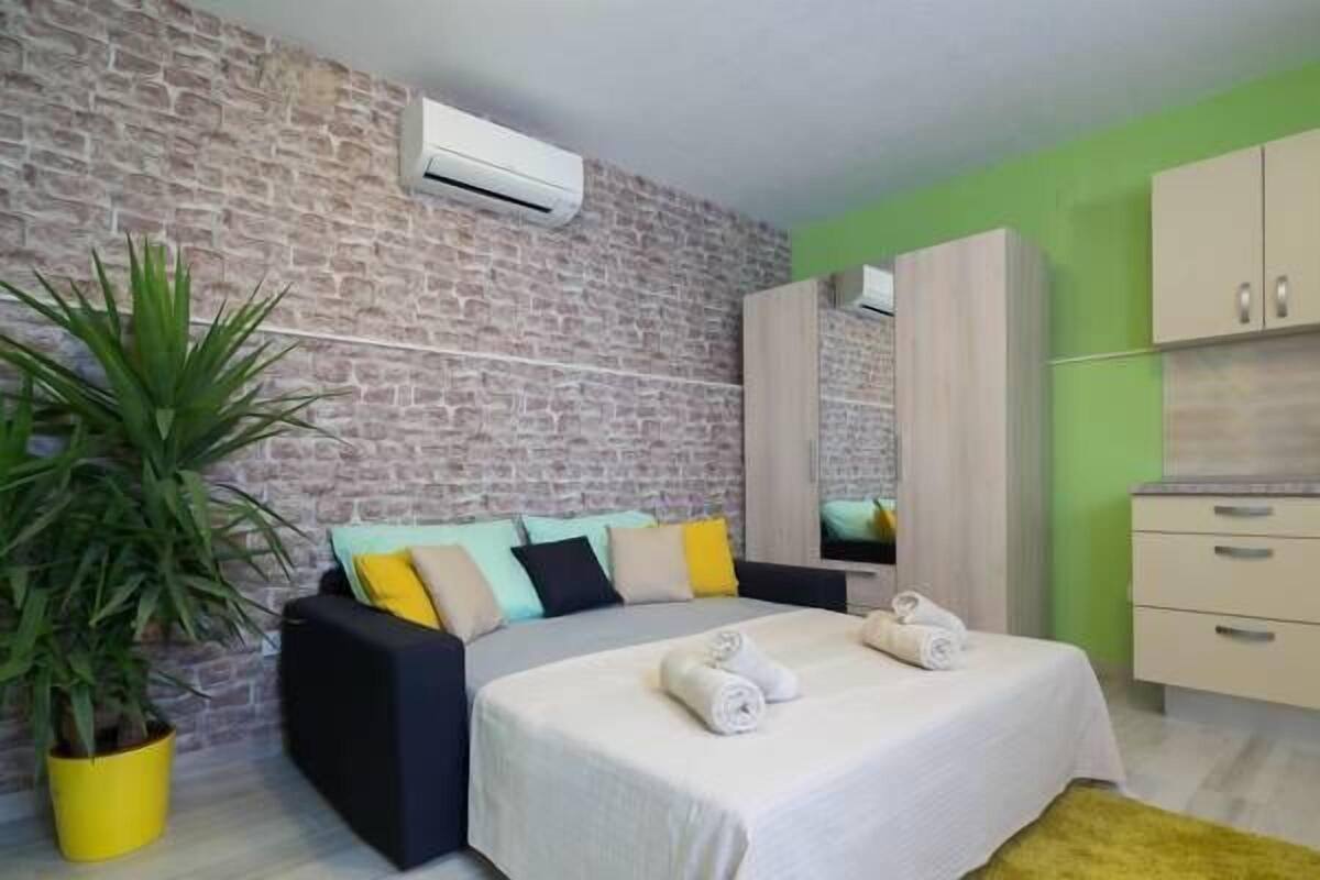 A modern bedroom with a brick-patterned wall, a bed with multiple pillows, a potted plant, and a wardrobe.