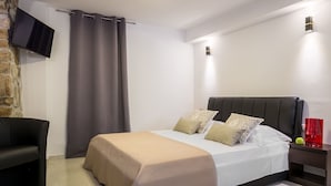 A modern bedroom with a bed, a TV mounted on a brick wall, and a nightstand with a red lamp. - Split Bliss Apartments (Split)