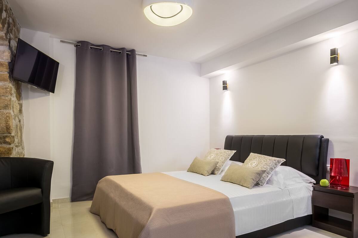 A modern bedroom with a bed, a TV mounted on a brick wall, and a nightstand with a red lamp.