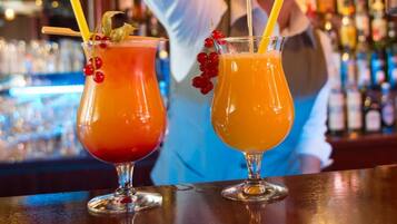 Two cocktails on a bar counter with a blurred background of bottles.