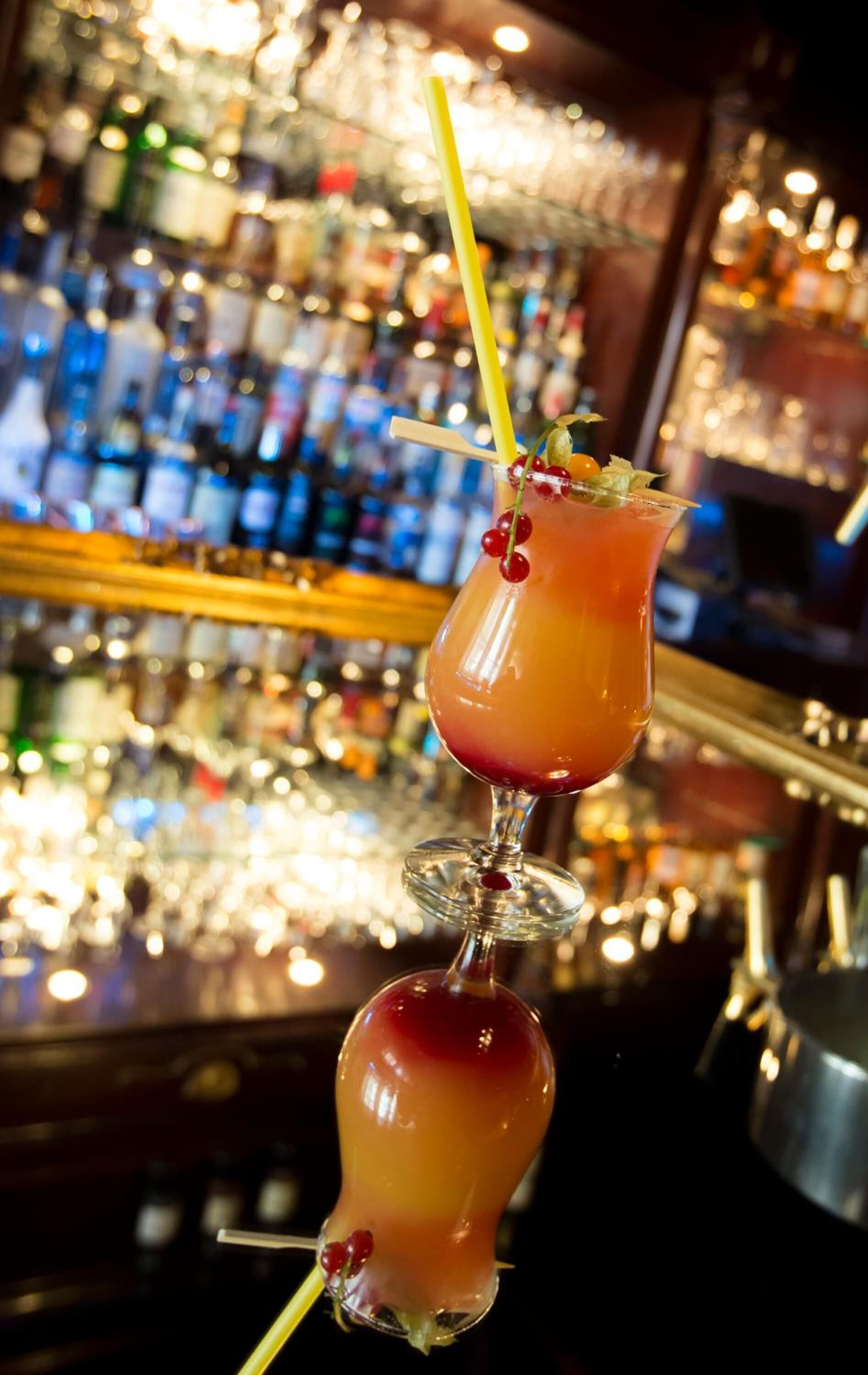 Deux cocktails décorés, un bar avec des étagères remplies de bouteilles et une lumière douce et chaleureuse.