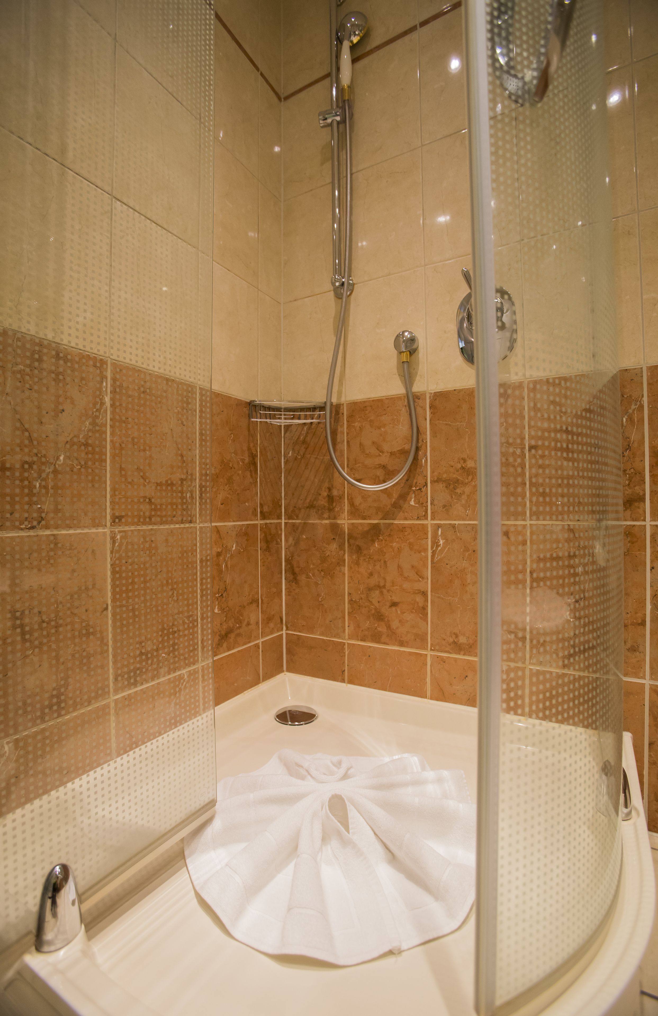 Ducha con puerta de cristal, cabezal de ducha manual y una toalla blanca en el suelo.