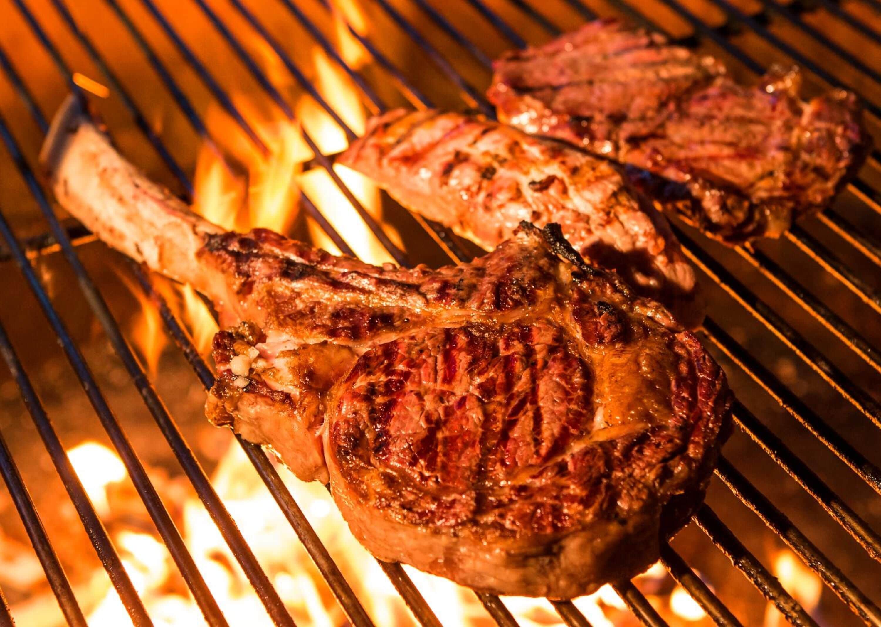 Zwei Steaks werden auf einem Grill über offenen Flammen zubereitet.