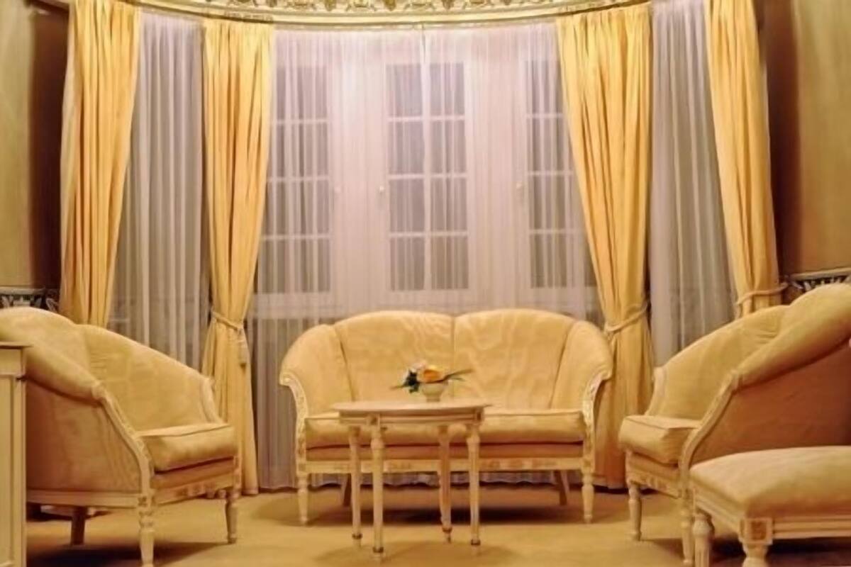 Um quarto com uma janela grande, duas poltronas, uma mesinha e um vaso decorativo.