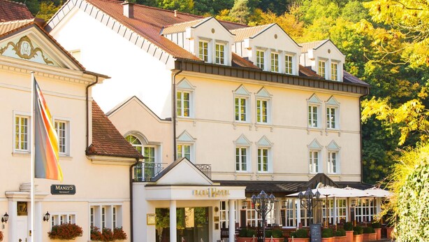 Un hôtel à la façade classique, avec un drapeau et une enseigne indiquant qu’il s’agit d’un hôtel.