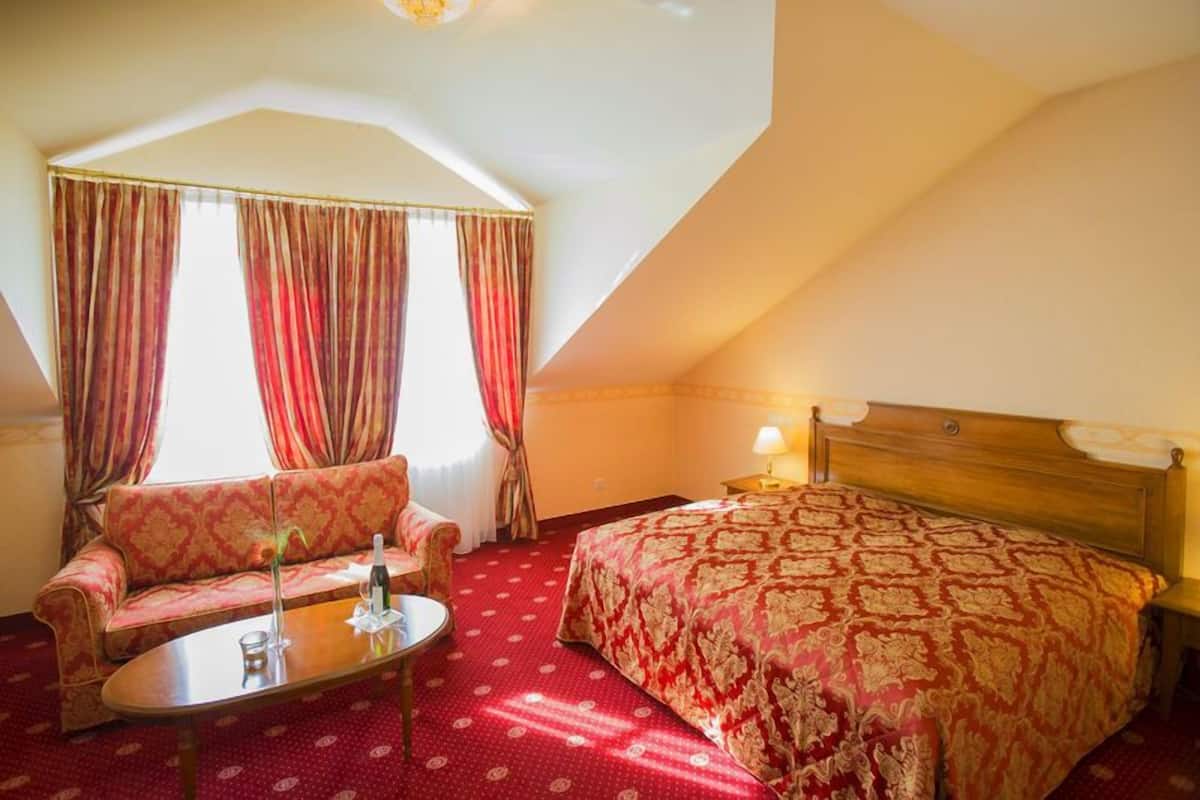 Quarto de hotel com cama, sofá, mesa e cortinas.