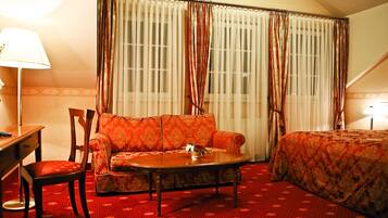 A hotel room with a sofa, a small table, a chair, a bed, and a window with curtains.