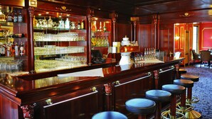 Un espace bar doté d’un comptoir en bois, de tabourets et d’étagères remplies de bouteilles et de verres.