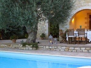An outdoor dining area with stone walls, wooden chairs, and a table set for two. - Vederi Estate (Rethymno)