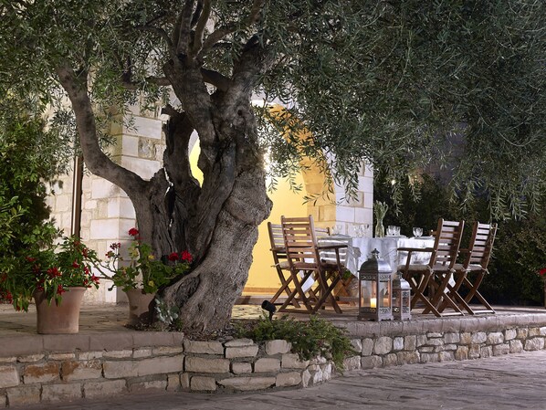 An outdoor dining area with a stone wall, wooden chairs, and a table set for two.