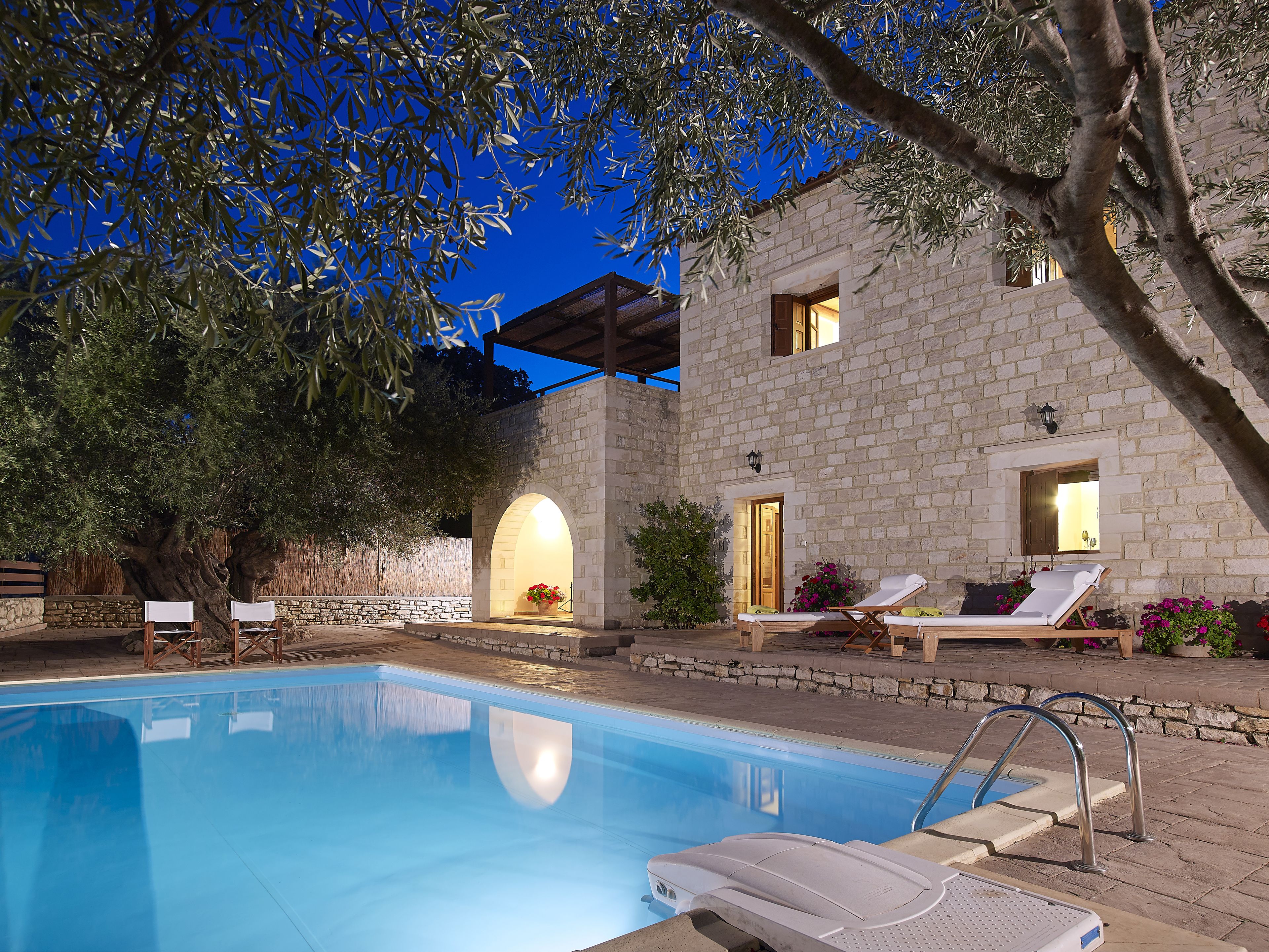 A pool area with lounge chairs and a stone building with arched doorways.