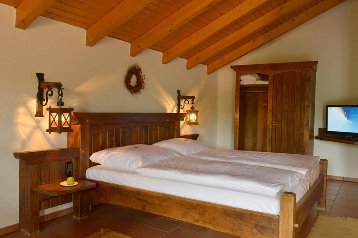 Uma cama de madeira com lençóis brancos em um quarto com vigas de madeira aparentes e uma televisão na parede.