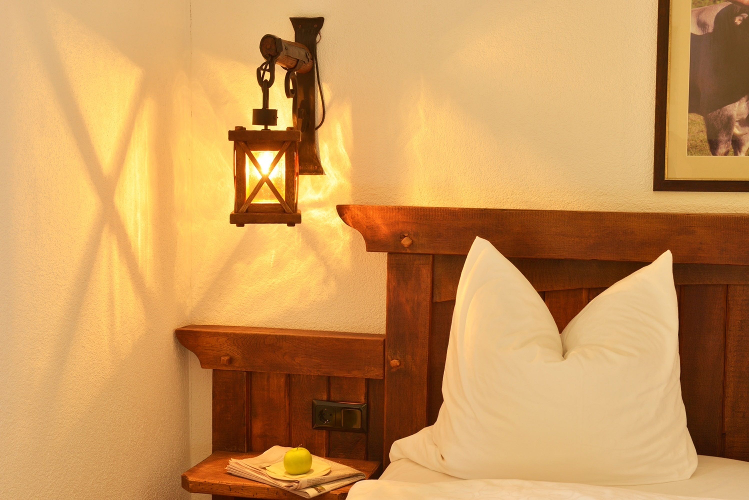 A bedroom with a wooden headboard, a bedside table with a lamp, and a framed picture on the wall.
