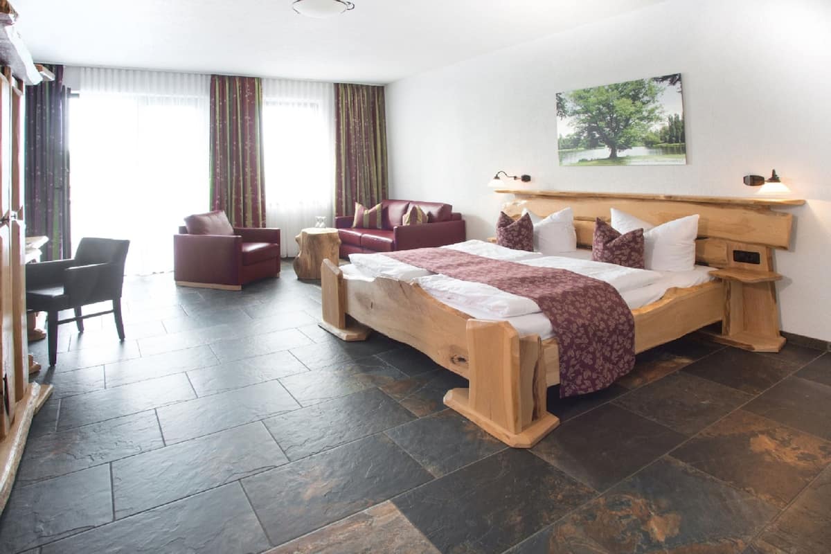 Quarto com cama grande, cabeceira de madeira, escrivaninha, cadeira e sofá.