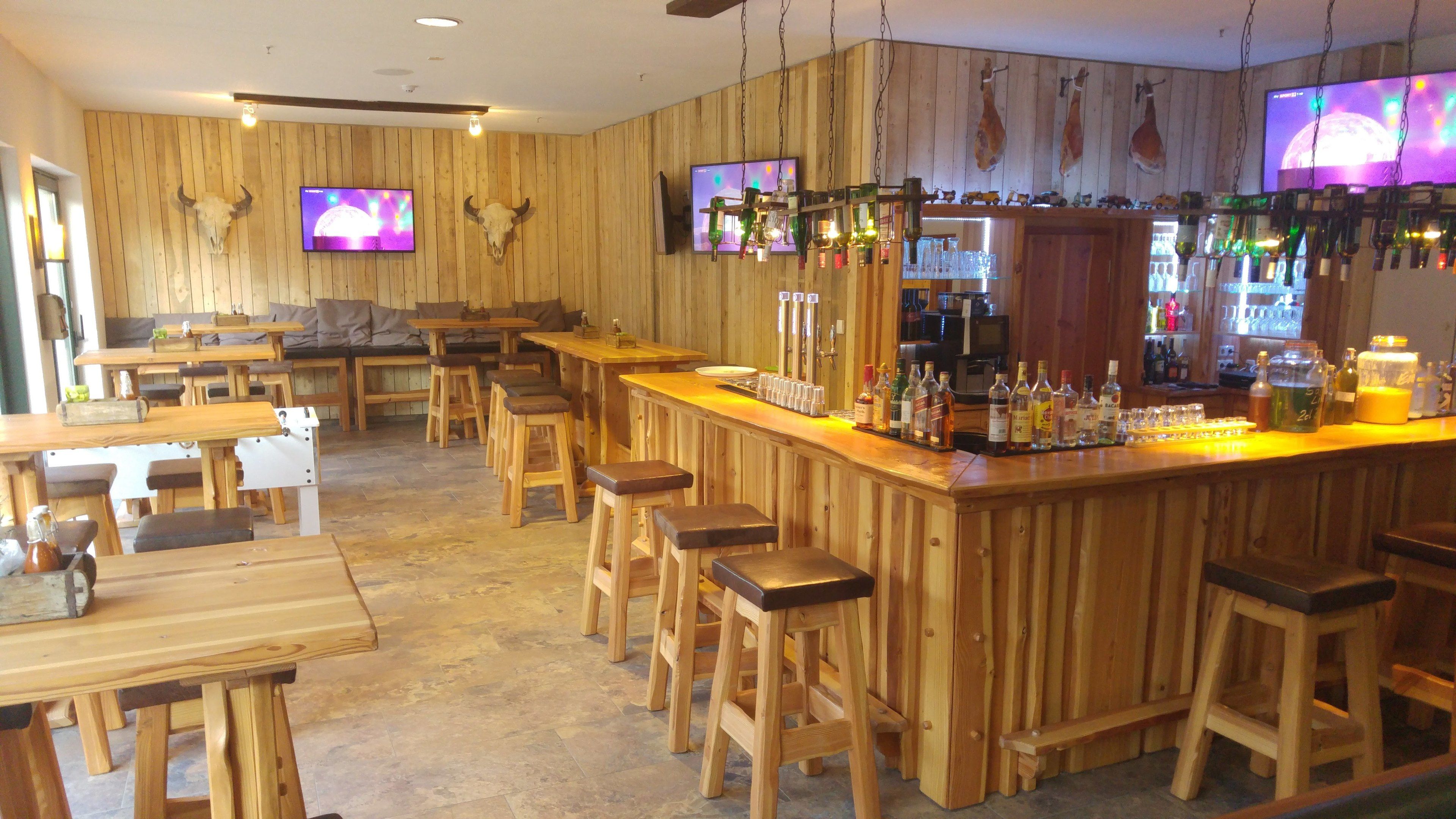 A rustic bar area with wooden furniture, a bar counter, stools, and mounted televisions.