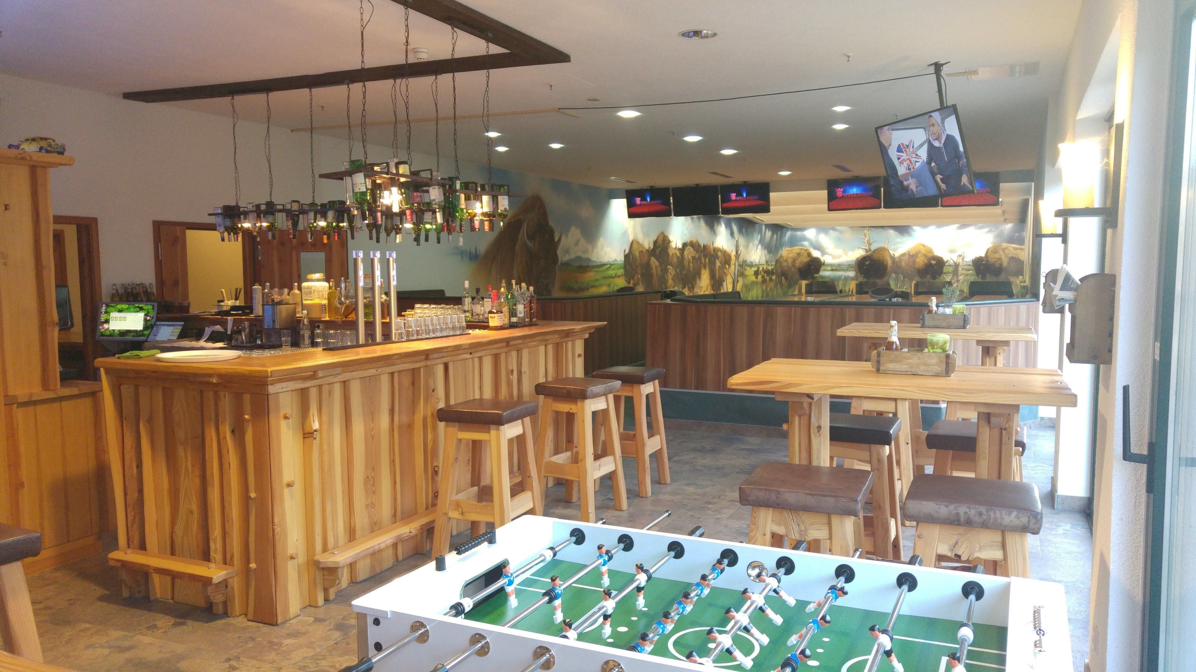 Zona de bar con taburetes, mesa de fútbol de mesa y un mural en la pared.