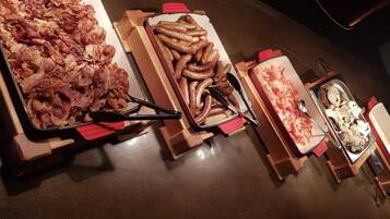 A buffet table with various food items including bacon, sausages, and a pizza.
