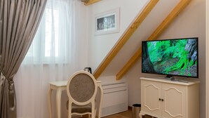 A room with a TV displaying a forest scene, a white cabinet, a chair, a radiator, and a window with curtains. - Priska Heritage Rooms (Split)