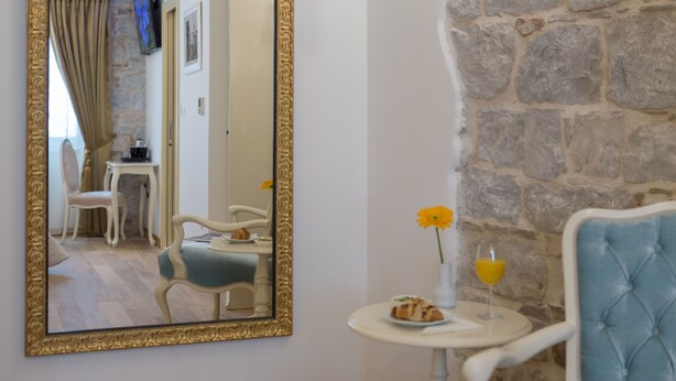 A room with a stone wall, a round table with a plate of food and a glass of orange juice, and a blue upholstered chair. - Priska Heritage Rooms (Split)
