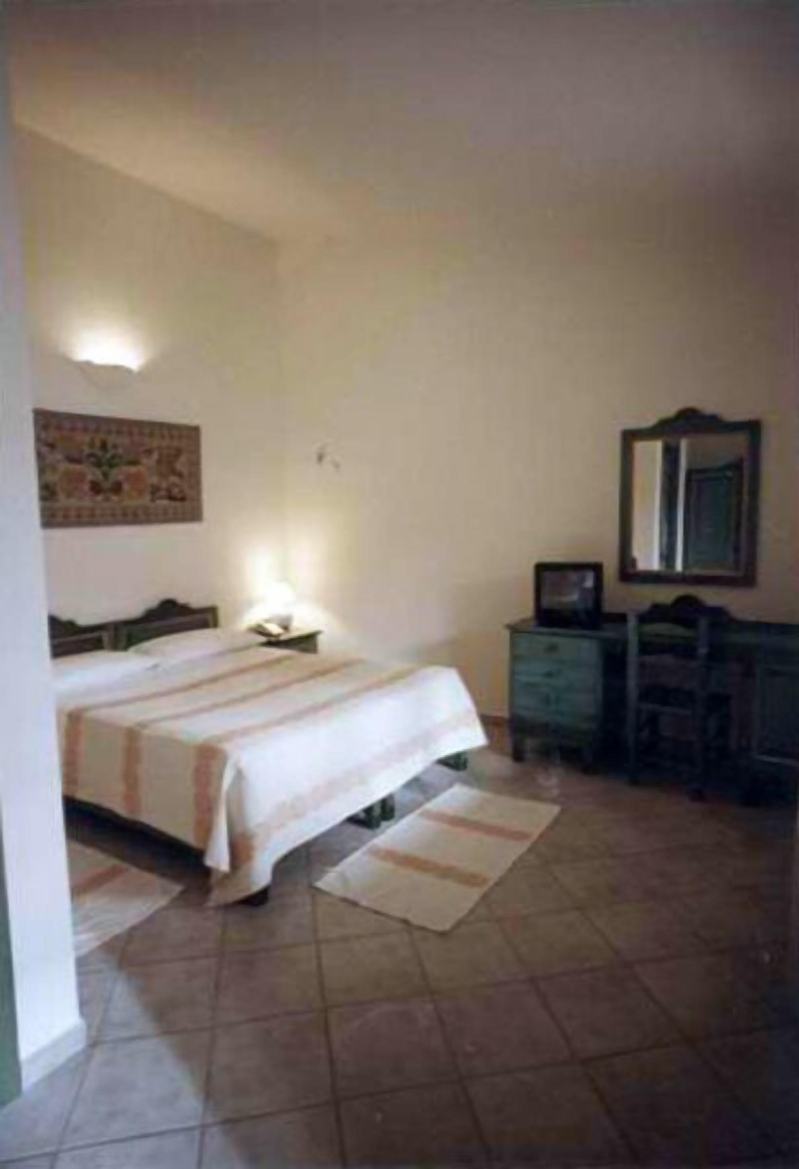 Una camera da letto con un letto, una cassettiera, uno specchio e una TV a parete.