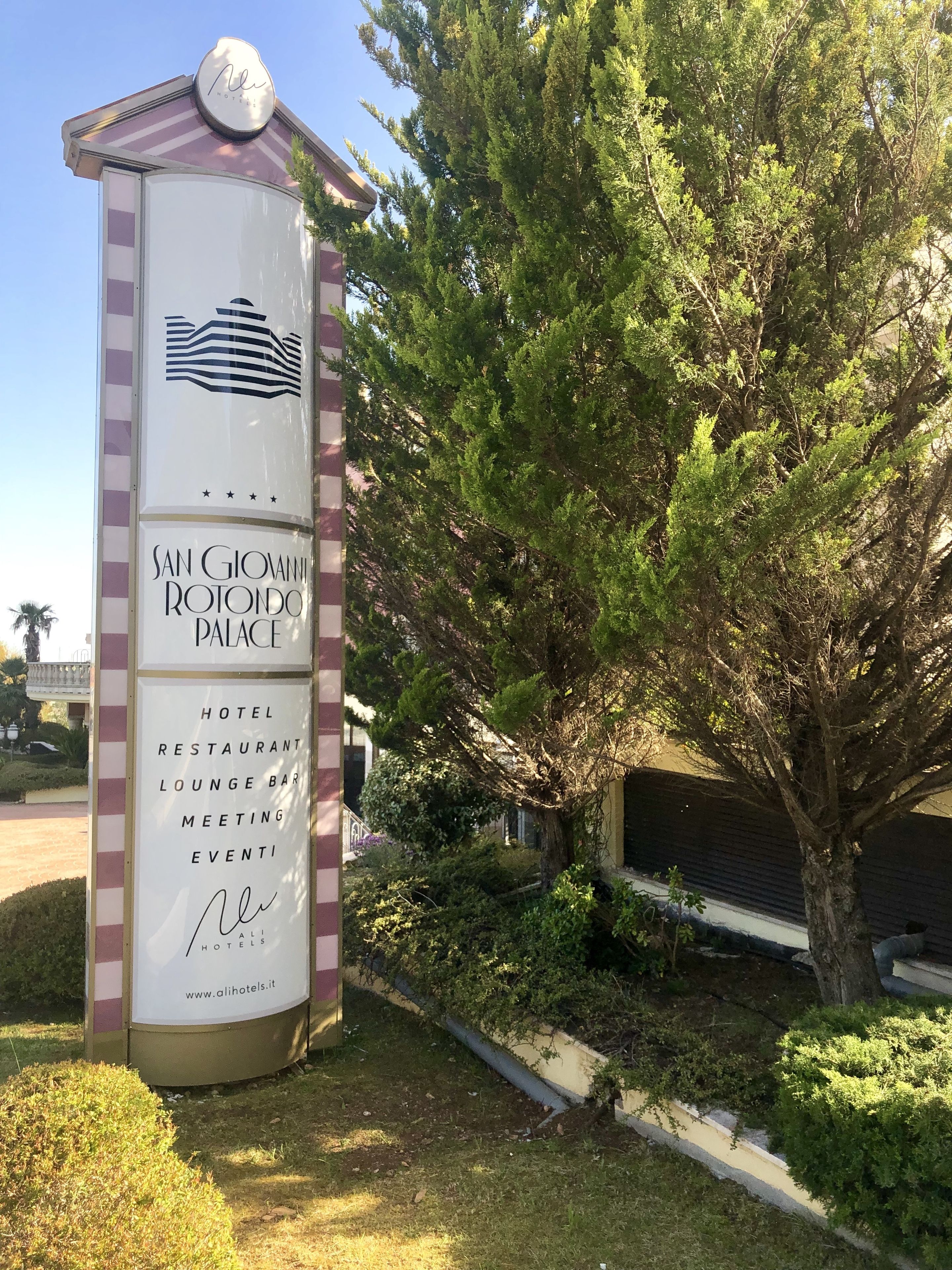 A sign for San Giovanni Rotondo Palace Hotel, listing amenities like a hotel, restaurant, lounge bar, meeting, and events.