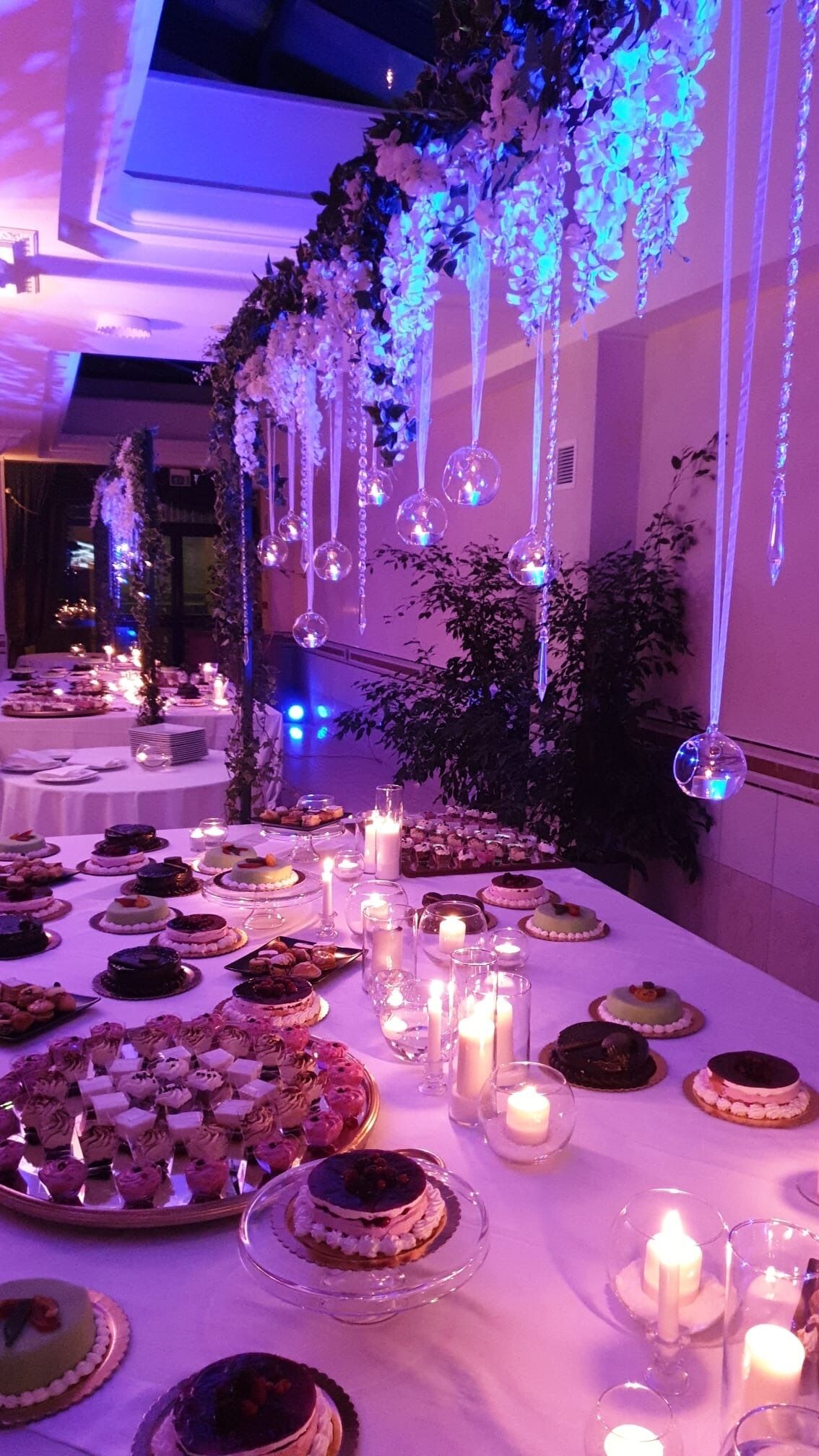 A banquet hall with tables set for a formal event, decorated with floral arrangements and hanging ornaments.