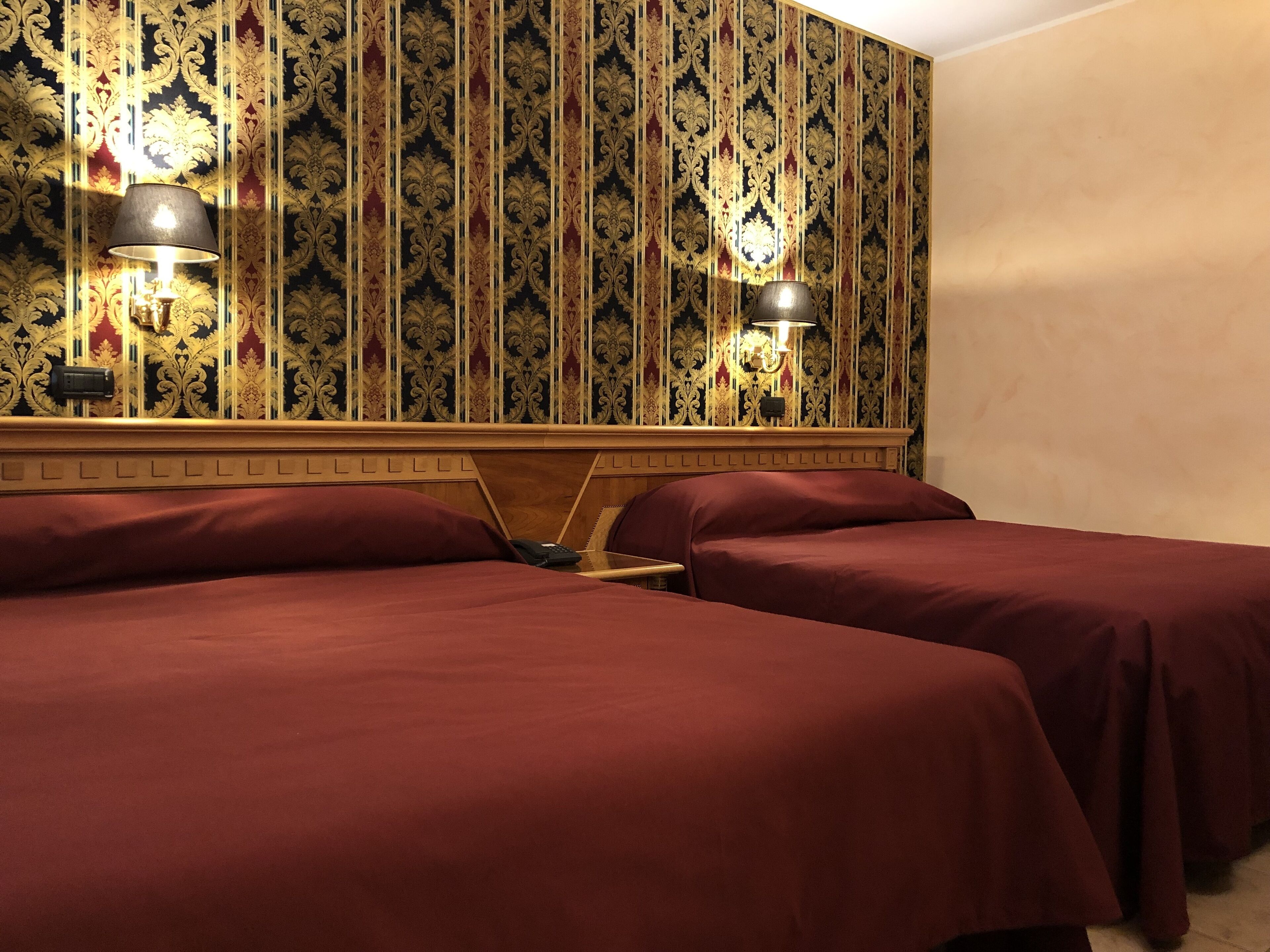 A hotel room with two beds, a wooden headboard, and a patterned wallpaper.