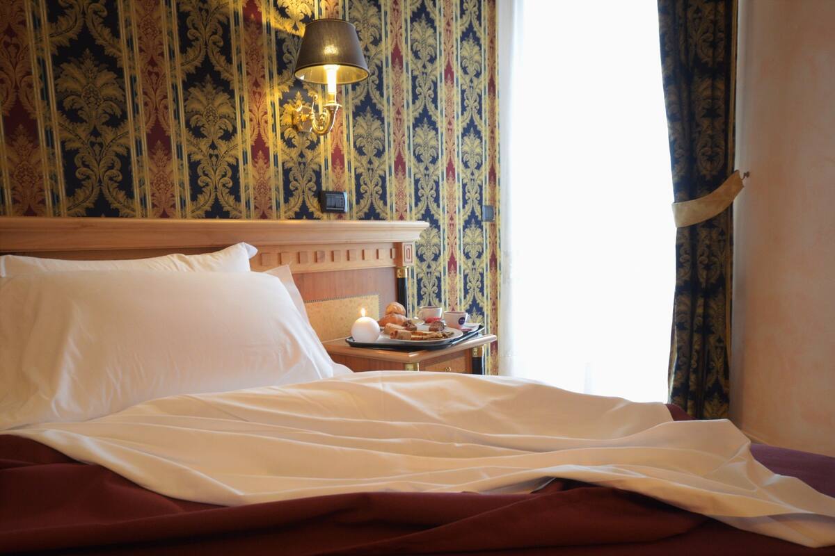 Ein Hotelzimmer mit einem ordentlich bezogenen Bett, einem Nachttisch mit Lampe und einem dekorativen Wandmuster.