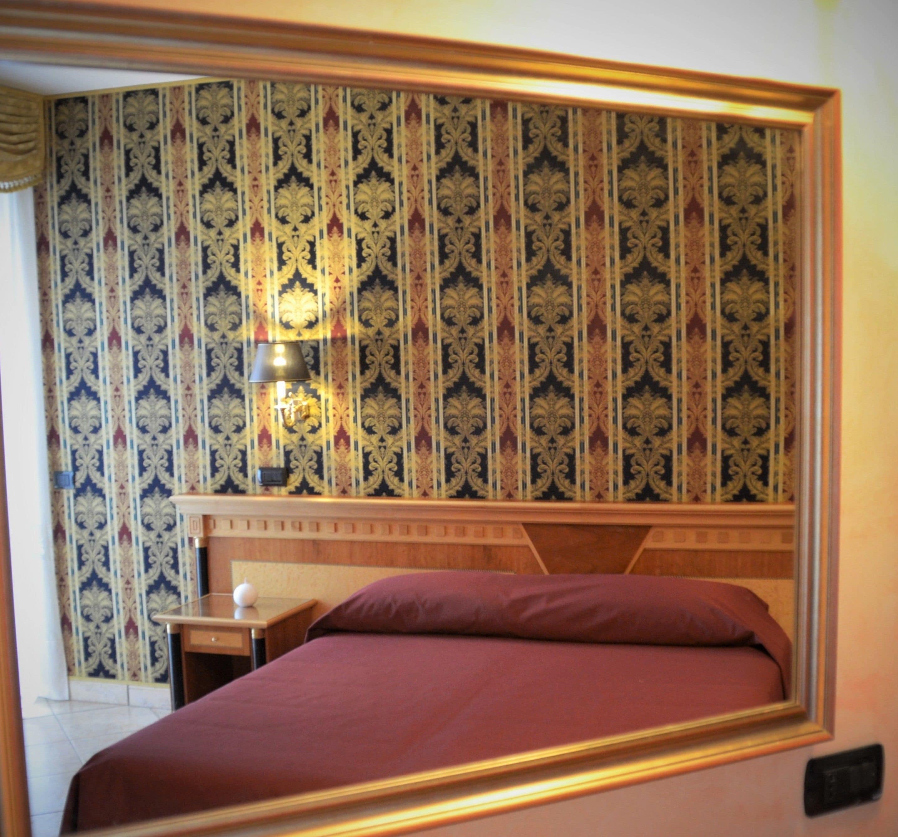 Un dormitorio con papel tapiz estampado, una mesita de noche con lámpara y una cama con cabecero.