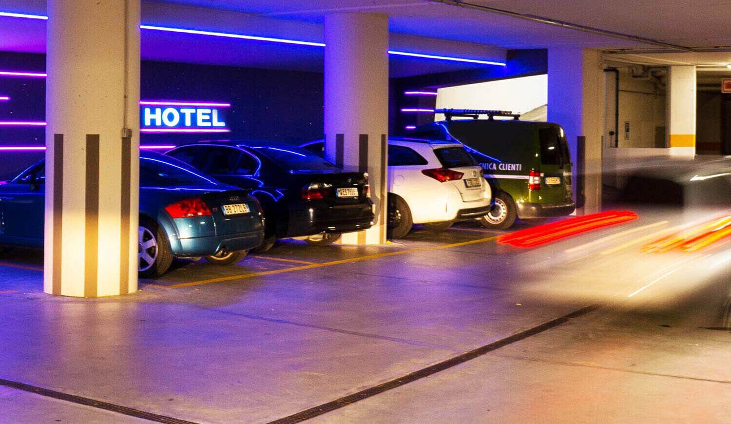 Un aparcamiento de hotel con varios coches estacionados bajo columnas iluminadas.