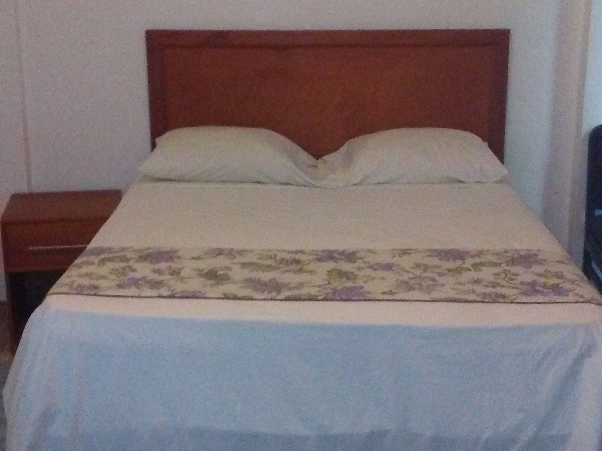 A bed with a wooden headboard, a floral bedspread, and a nightstand to the left.