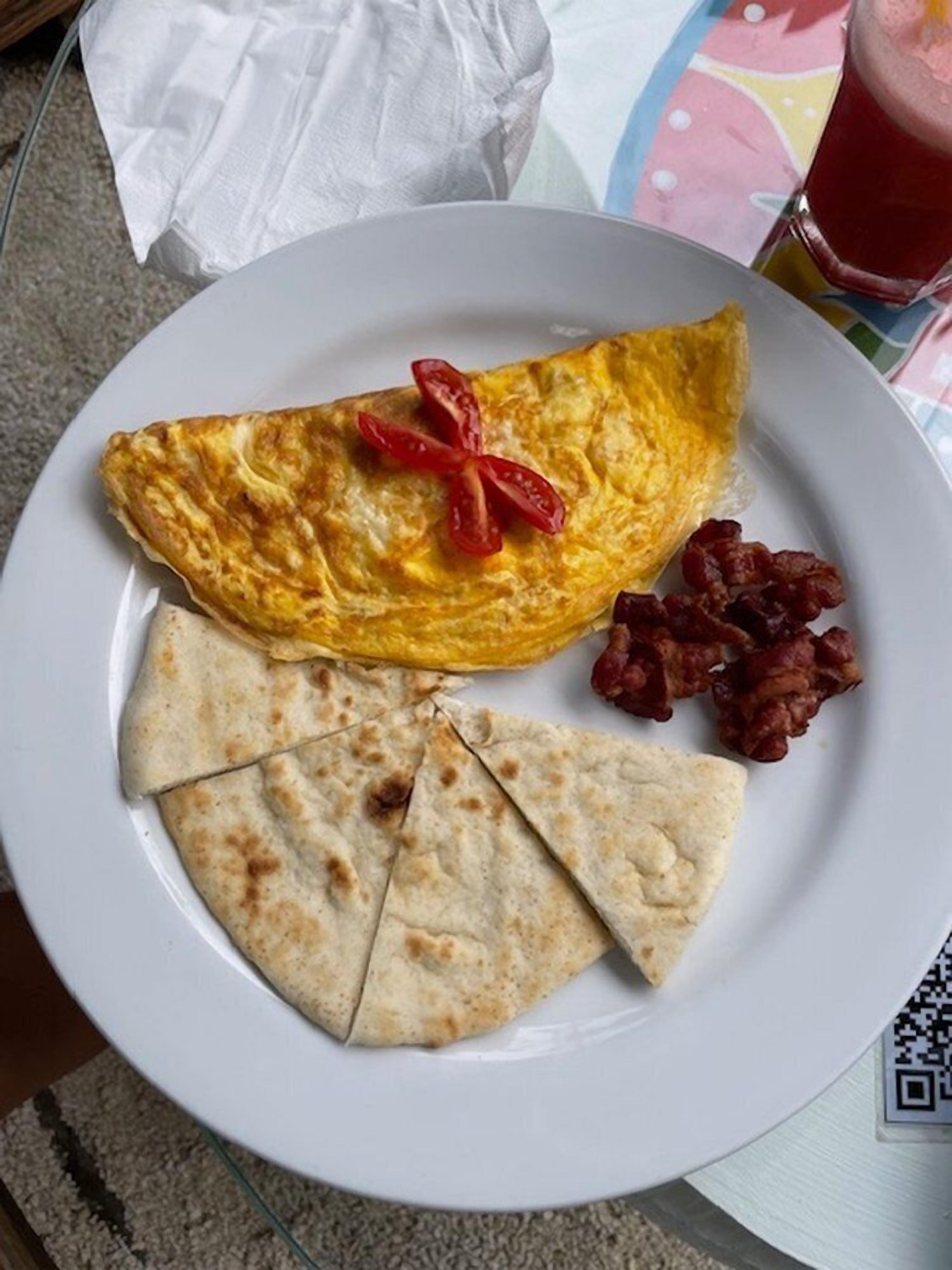 Un plato con tortilla, tortillas rebanadas y carne cocida, posiblemente tocino, sobre una mesa con servilleta blanca y un vaso de bebida roja.