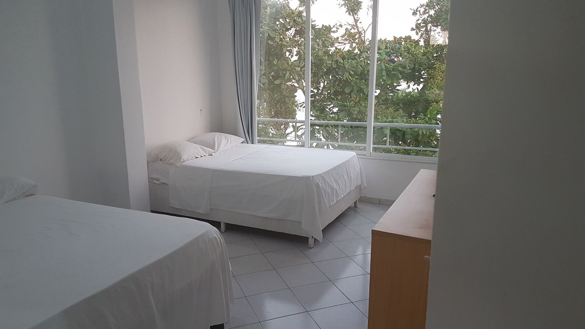 A bedroom with two beds, a window with a view of trees, and a small table.