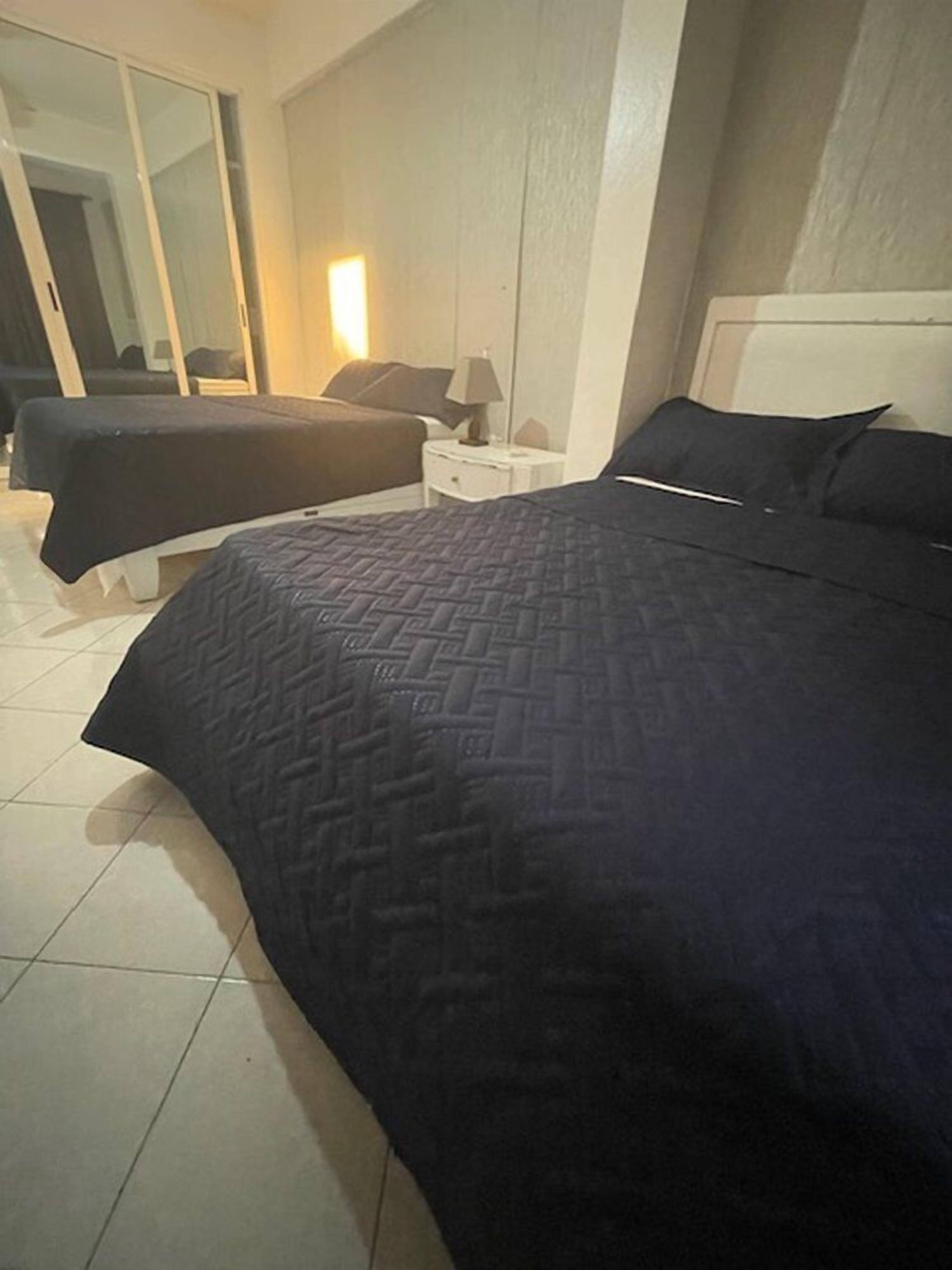 A hotel room with two beds, a nightstand, a lamp, and a large mirror.
