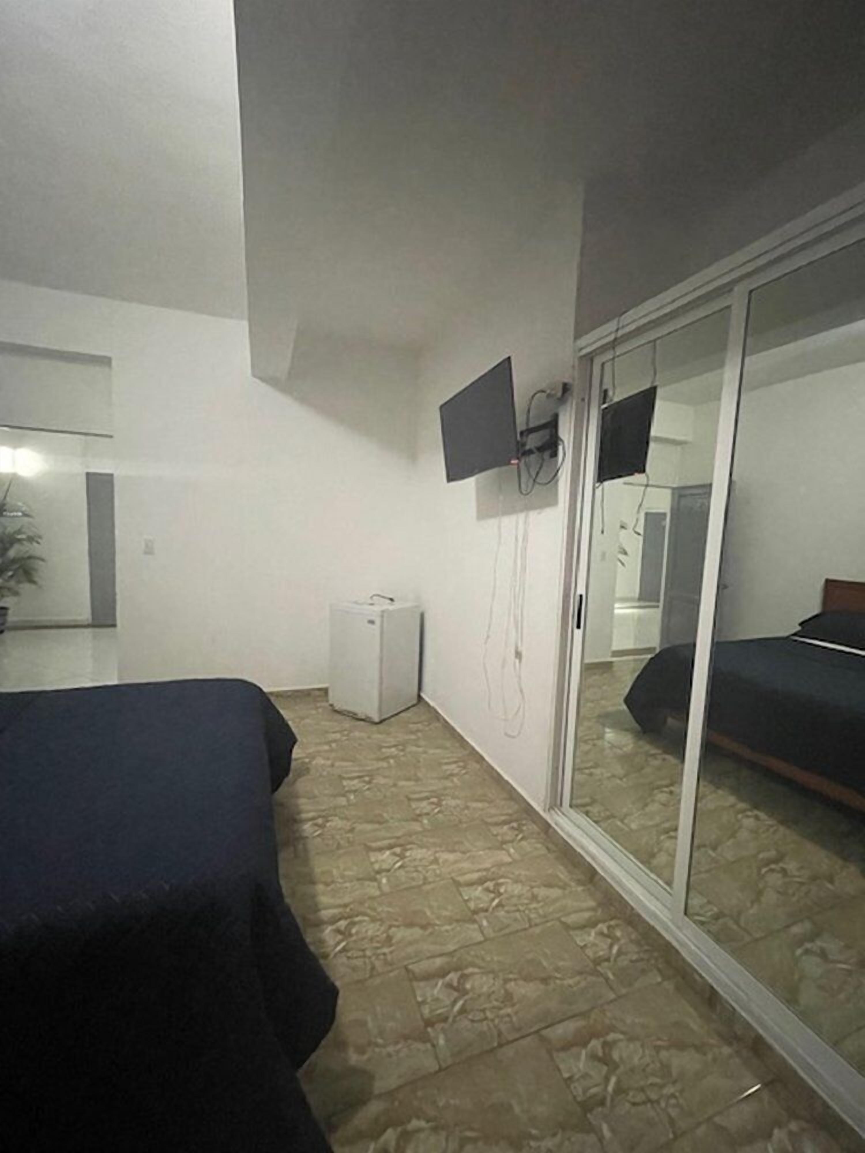 Une chambre d’hôtel avec un lit, une petite glacière blanche, un téléviseur fixé au mur et une porte coulissante en verre donnant sur la salle de bain.