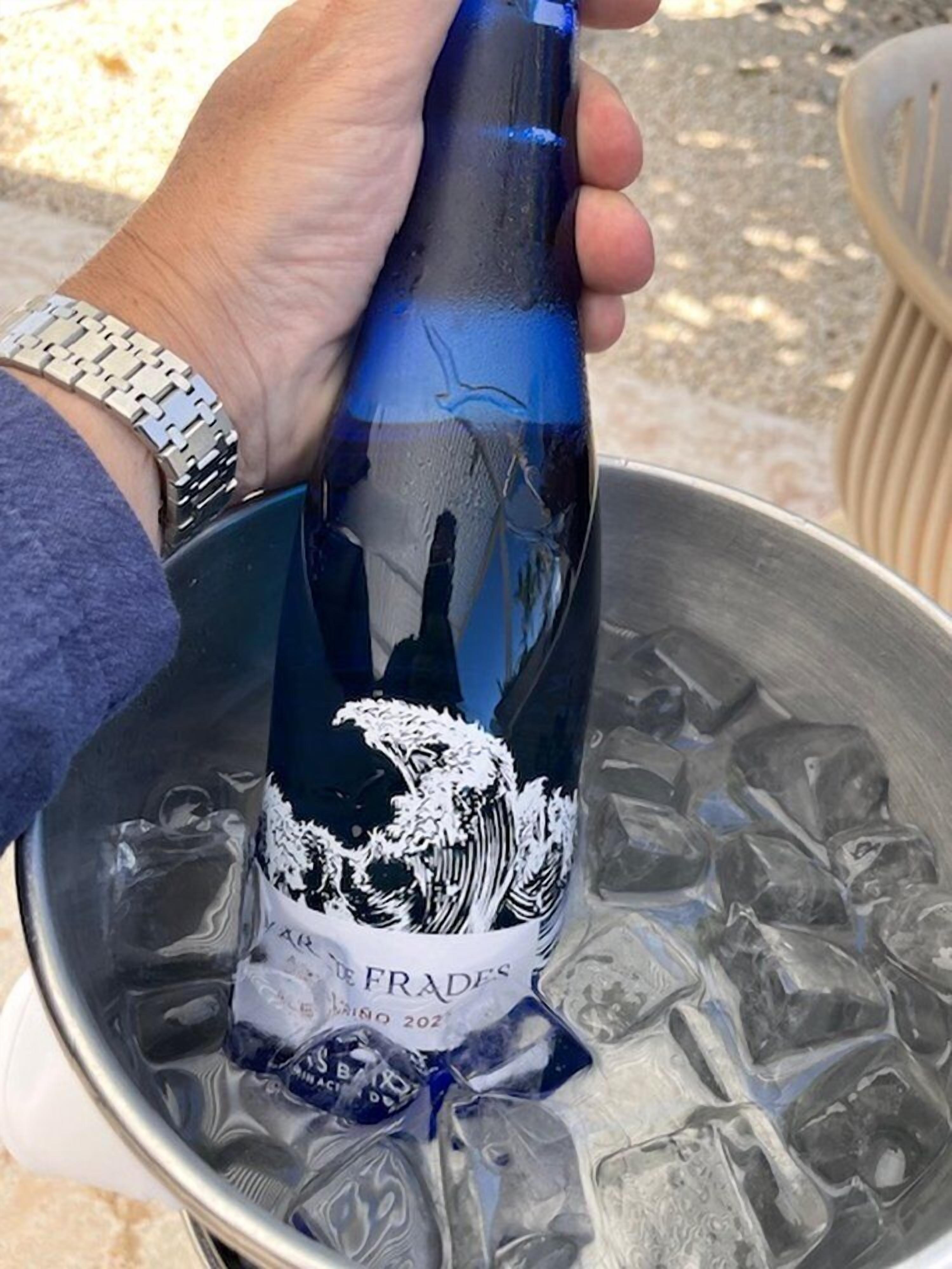 A hand holding a bottle with a wave design and text, over a bucket of ice.