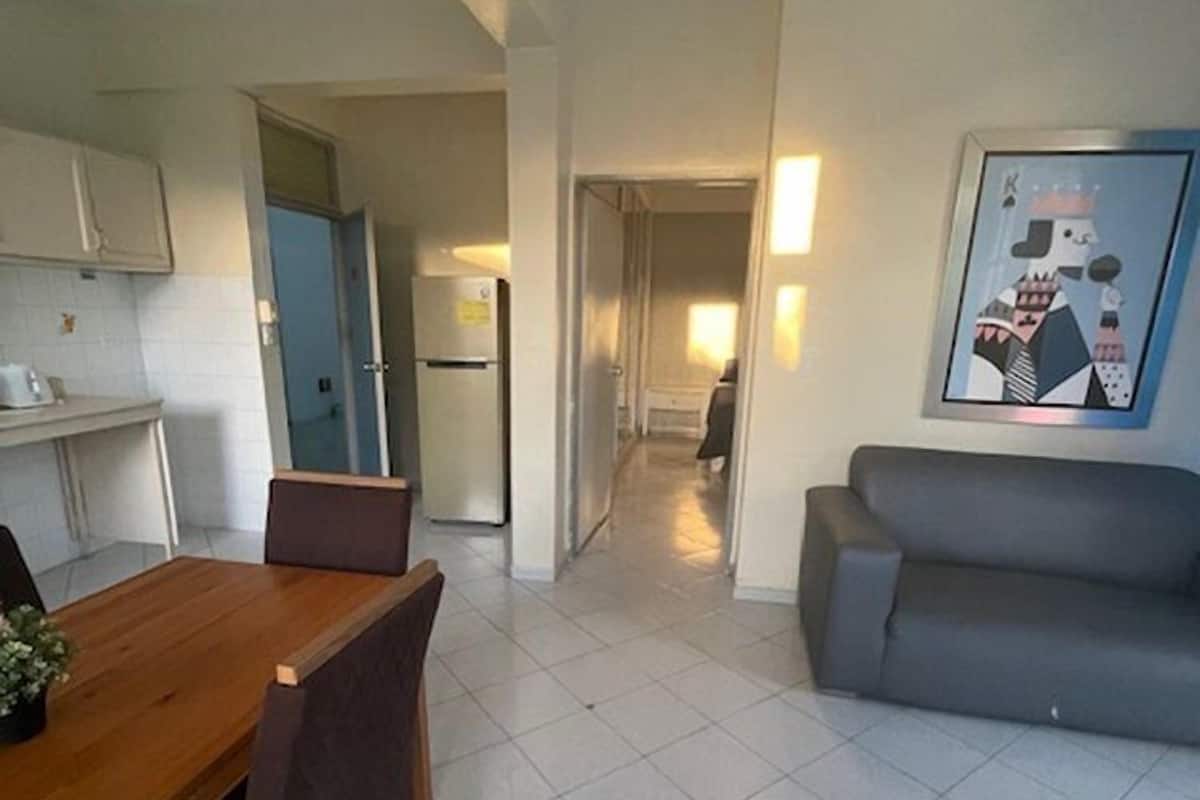Un apartamento moderno con comedor, un sofá gris y cocina.