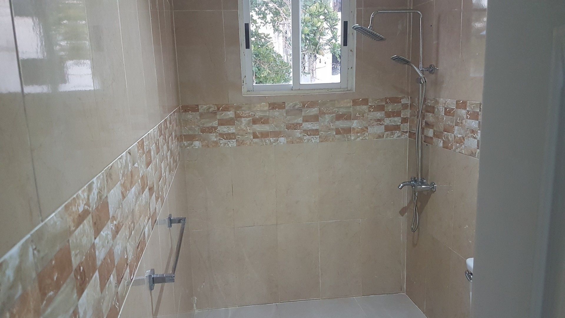 A bathroom with a shower, a window, and a tiled wall with a brick pattern.