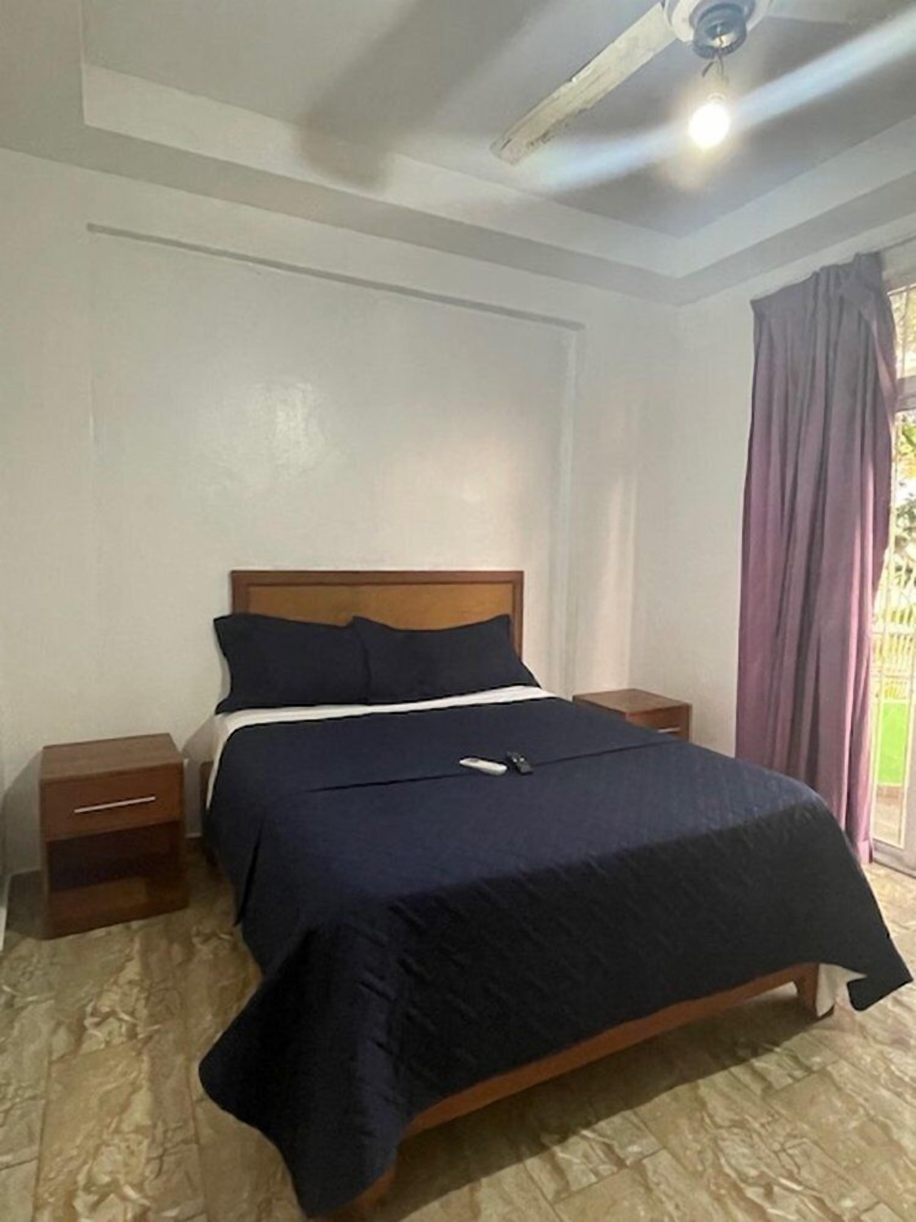 Un dormitorio con una cama, cabecera de madera, dos mesitas de noche y un ventilador de techo.