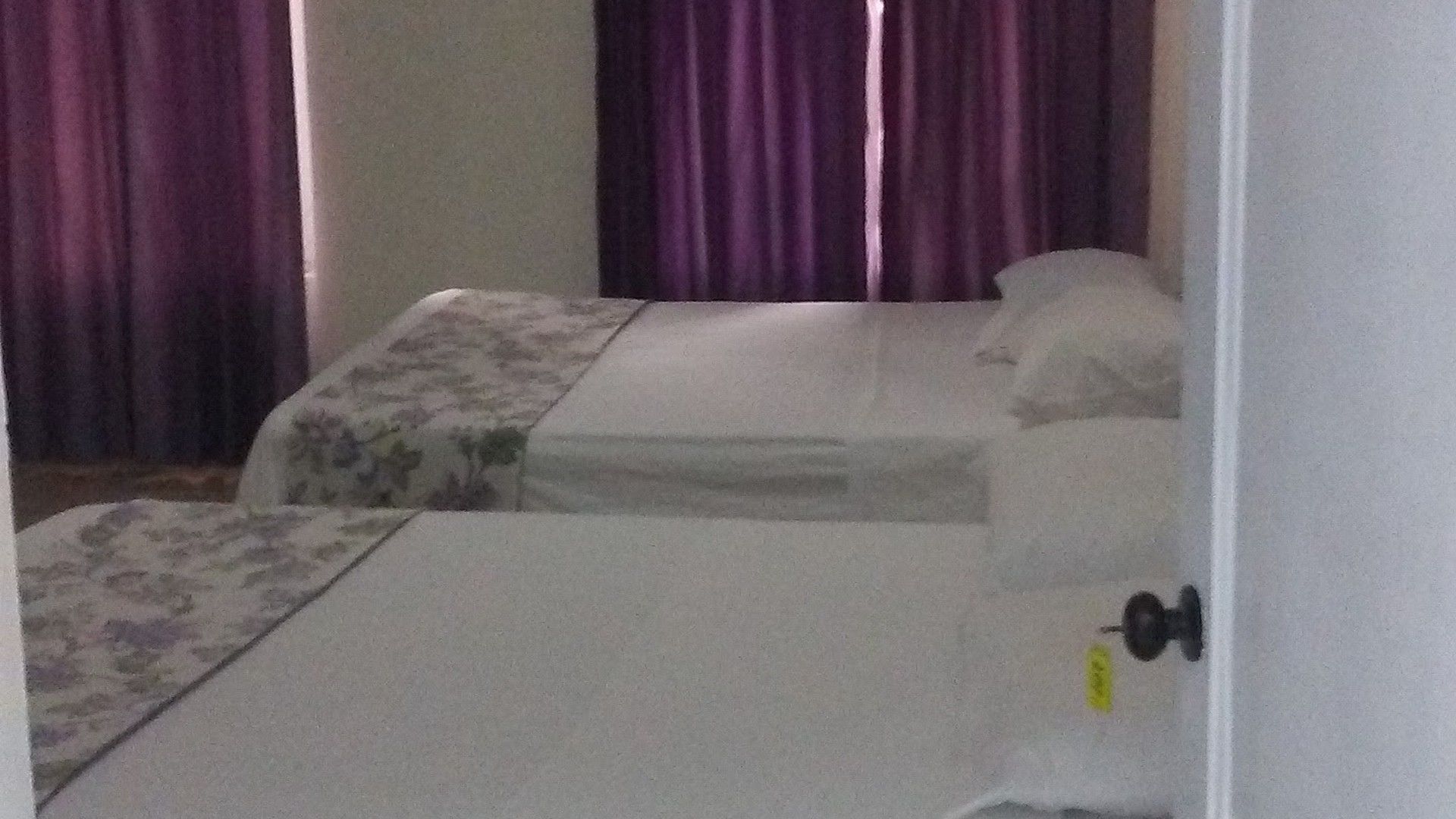Une petite chambre individuelle avec deux lits, une porte et des rideaux violets.