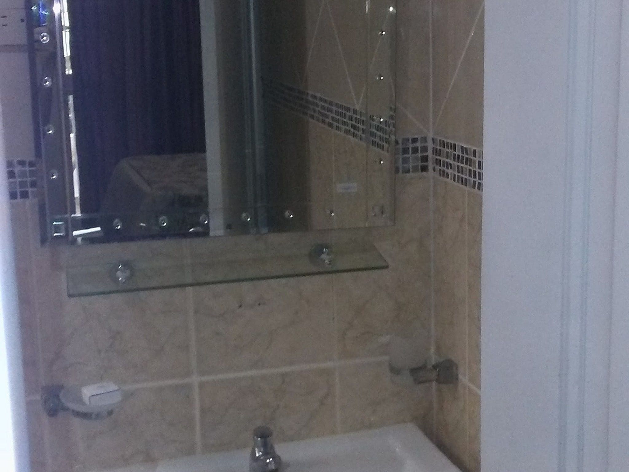 A bathroom with a glass shelf, a mirror, a sink, and tiled walls.