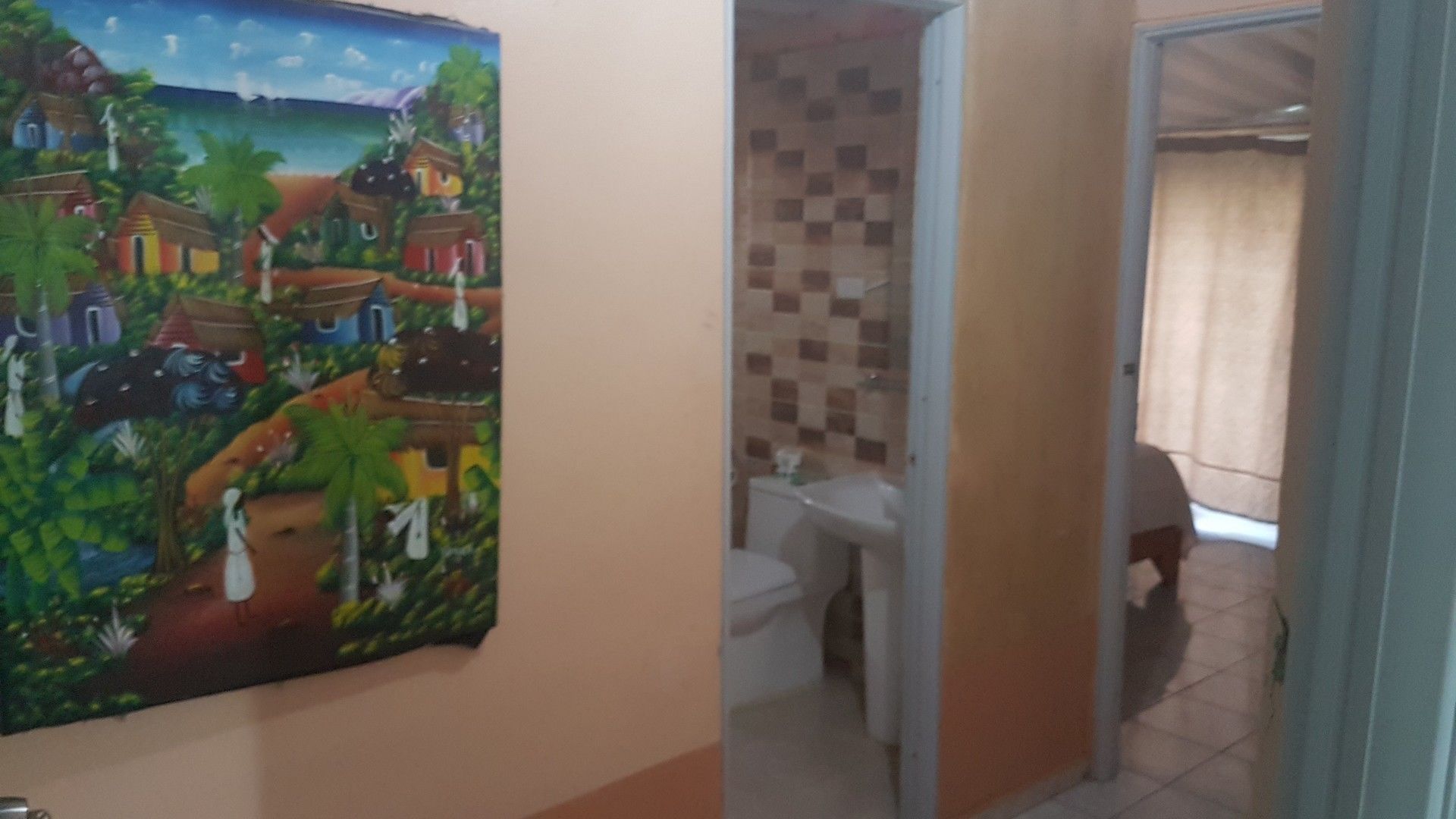A room with a colorful mural, a bathroom with a tiled wall, and a view of the outside.