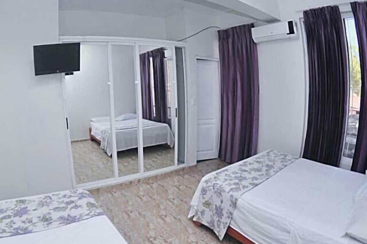 Een slaapkamer met twee bedden, een televisie en een schuifdeur die naar een andere kamer leidt.