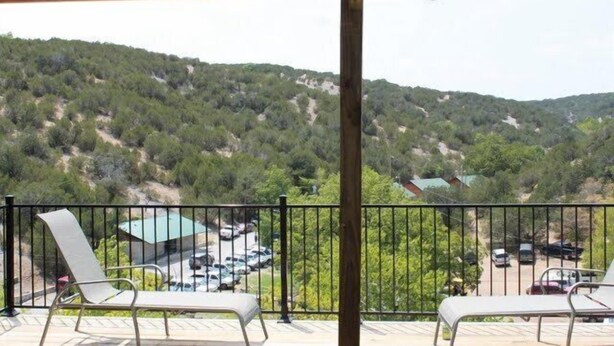 A balcony with two lounge chairs, a view of a parking area, and a building in the background. - Turner Falls (Davis)