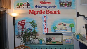 A wall mural with 'Myrtle Beach' and 'The Midtown' text, a lamp, a fish tank, and a small plant. - Midtown Cottages (Myrtle Beach)