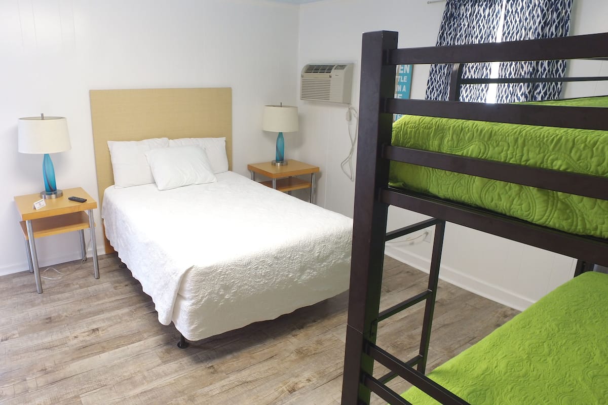 A hotel room with a single bed, two bedside tables with lamps, a bunk bed, and a patterned curtain.