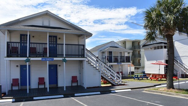 A motel with a two-story structure, a covered porch, and a staircase leading to the upper level. - Midtown Cottages (Myrtle Beach)