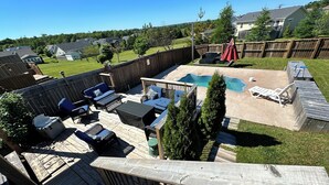 Um quintal com piscina, móveis de exterior e um deck de madeira.