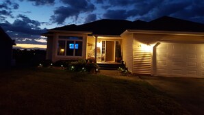 Uma casa residencial ao entardecer, com garagem, porta visível e pequeno alpendre.