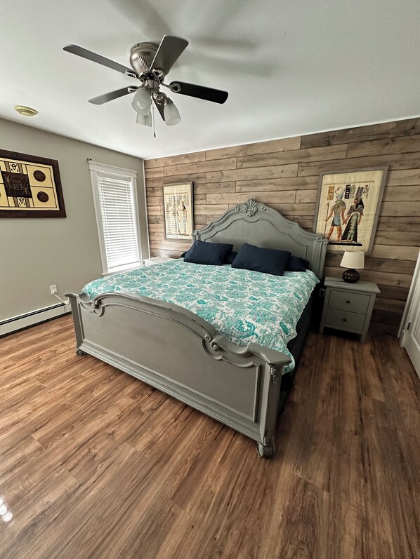 Une chambre à coucher avec un lit, un ventilateur de plafond, des lambris en bois et des œuvres d’art.